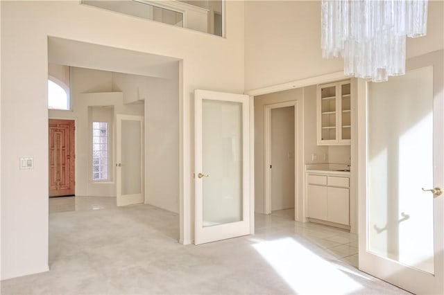 interior space featuring french doors, a towering ceiling, light colored carpet, and a notable chandelier