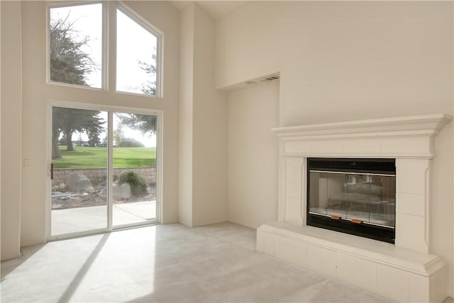 unfurnished living room featuring a tile fireplace, a towering ceiling, and a wealth of natural light