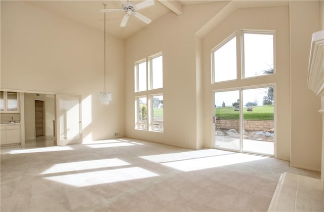 unfurnished living room featuring beamed ceiling, ceiling fan with notable chandelier, light colored carpet, and high vaulted ceiling