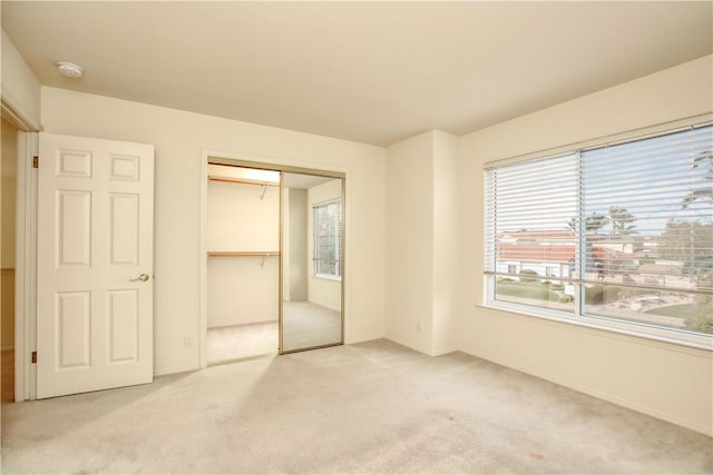 unfurnished bedroom with multiple windows, light carpet, and a closet