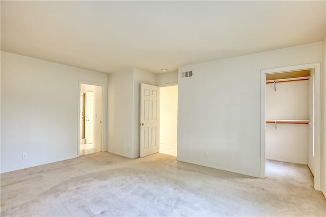 unfurnished bedroom with a spacious closet, a closet, and light carpet