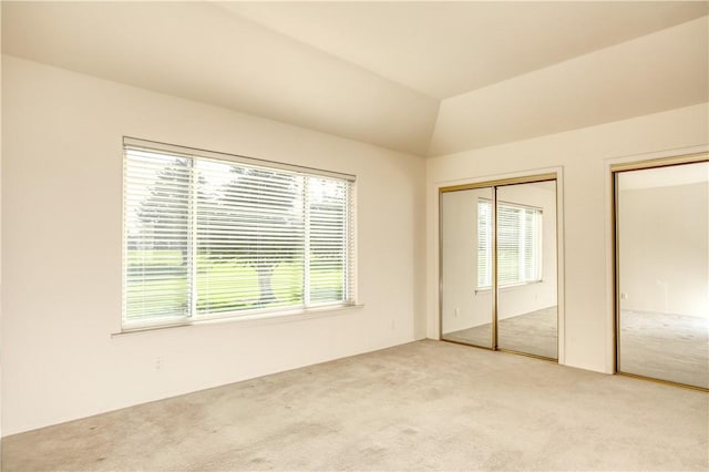 unfurnished bedroom with multiple closets, light colored carpet, multiple windows, and lofted ceiling