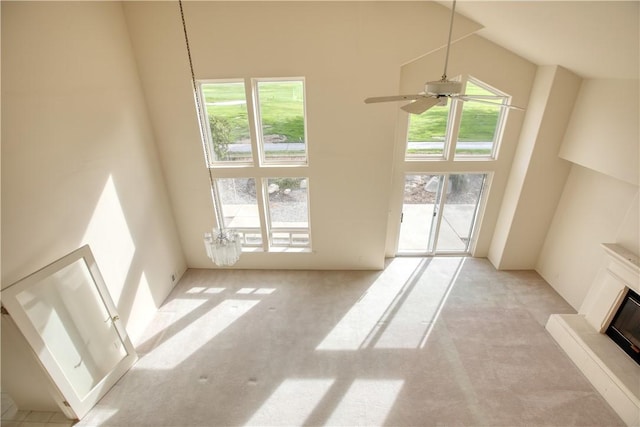 unfurnished living room with light carpet, ceiling fan with notable chandelier, and a high ceiling