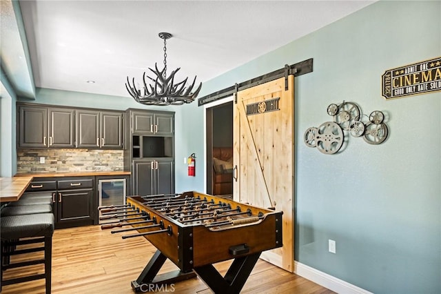 game room with a barn door, light hardwood / wood-style flooring, wine cooler, and a notable chandelier