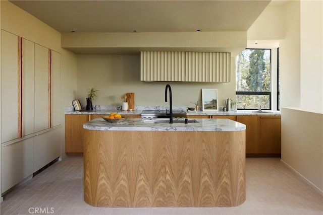 kitchen with a kitchen island with sink, sink, and light stone counters