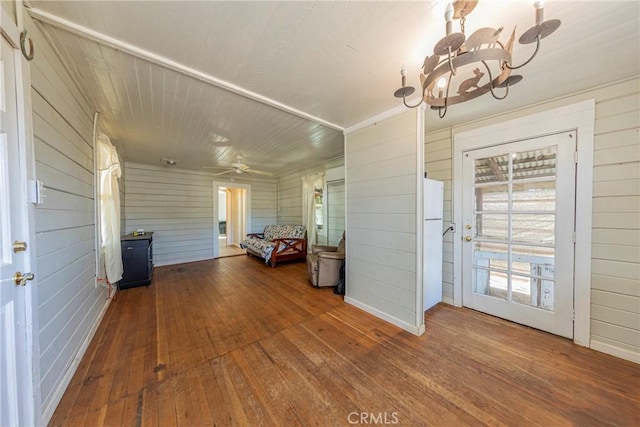 interior space with hardwood / wood-style flooring, ceiling fan with notable chandelier, and wooden walls