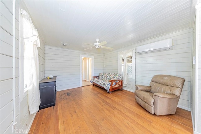 sitting room featuring wooden walls, ceiling fan, light wood-type flooring, and a wall unit AC