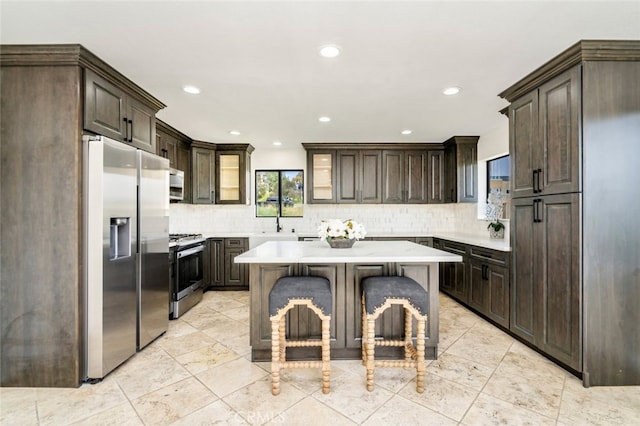 kitchen featuring light countertops, appliances with stainless steel finishes, dark brown cabinetry, and a center island