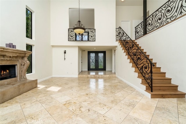 foyer entrance featuring baseboards, a fireplace, stairway, and french doors