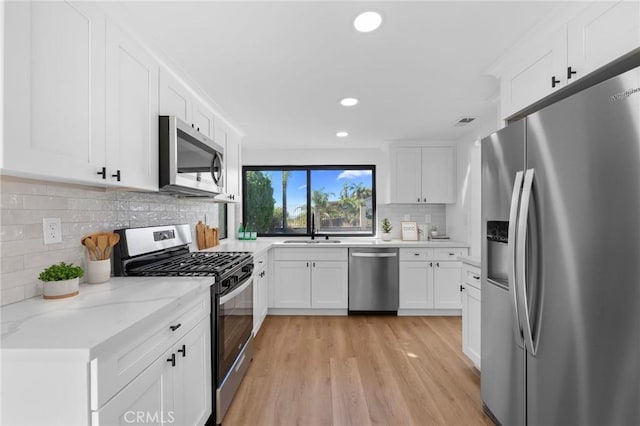 kitchen with sink, light hardwood / wood-style flooring, decorative backsplash, white cabinets, and appliances with stainless steel finishes