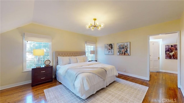 bedroom with vaulted ceiling, an inviting chandelier, and hardwood / wood-style floors