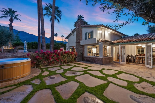 back house at dusk featuring a mountain view, a patio, and a hot tub