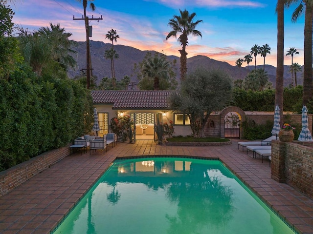 pool at dusk featuring a mountain view and a patio