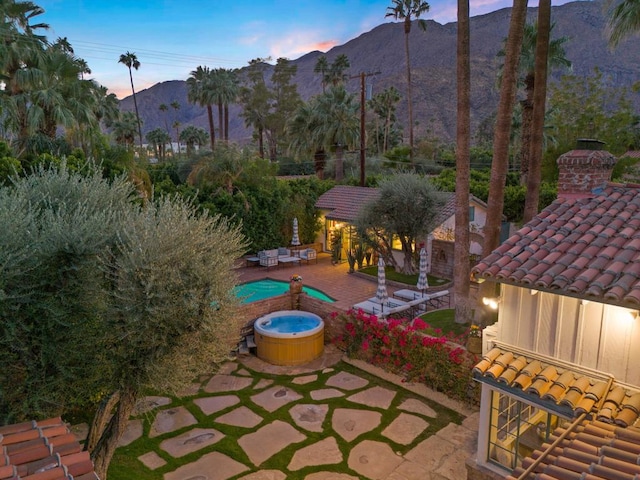 patio terrace at dusk with a mountain view and a swimming pool with hot tub