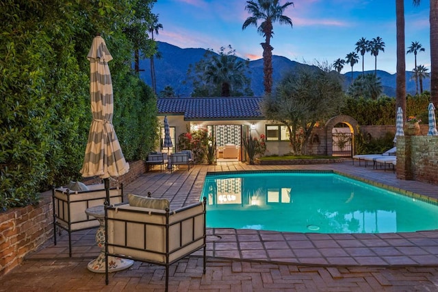 pool at dusk featuring a mountain view and a patio