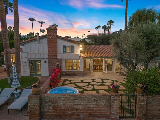 back house at dusk featuring a hot tub, a patio, and french doors