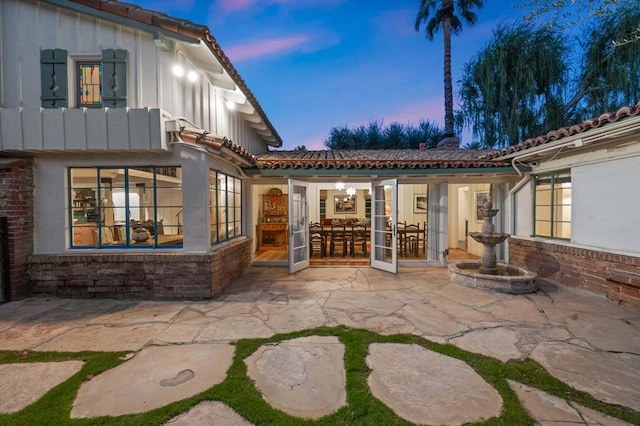 back house at dusk featuring french doors and a patio area