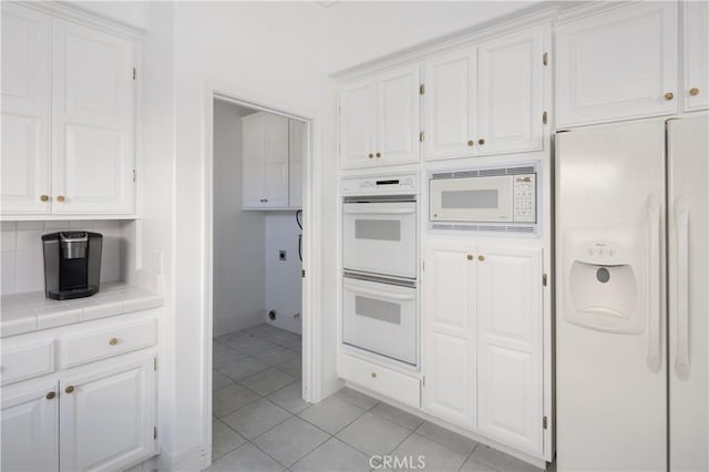 kitchen featuring tile countertops, white appliances, light tile patterned floors, tasteful backsplash, and white cabinetry