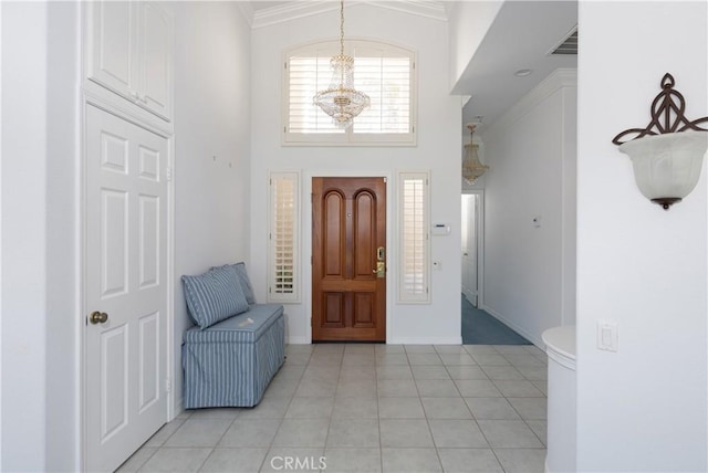 tiled entryway featuring a towering ceiling, an inviting chandelier, and crown molding