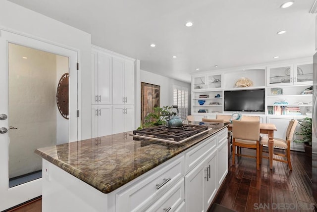 kitchen featuring dark hardwood / wood-style floors, a center island, stainless steel gas stovetop, white cabinets, and dark stone counters