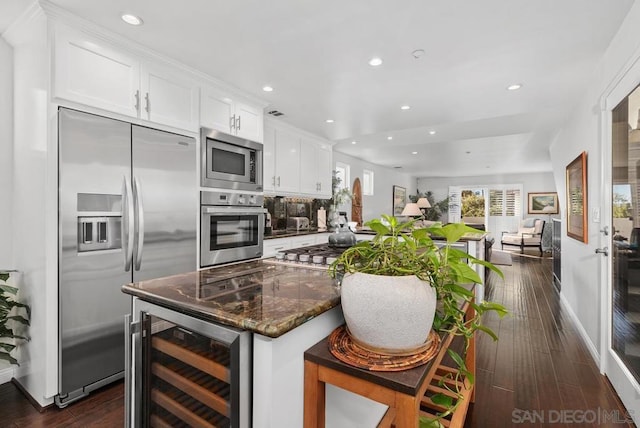 kitchen featuring beverage cooler, a breakfast bar area, built in appliances, dark stone counters, and white cabinets