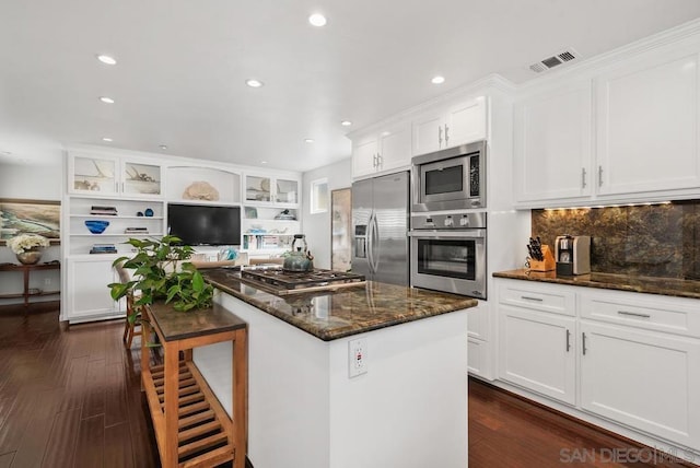 kitchen featuring appliances with stainless steel finishes, white cabinetry, dark stone countertops, tasteful backsplash, and dark wood-type flooring