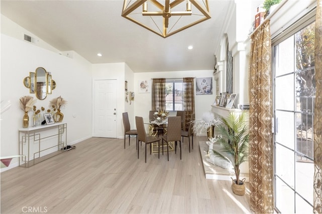 dining space with light wood-type flooring, an inviting chandelier, and vaulted ceiling