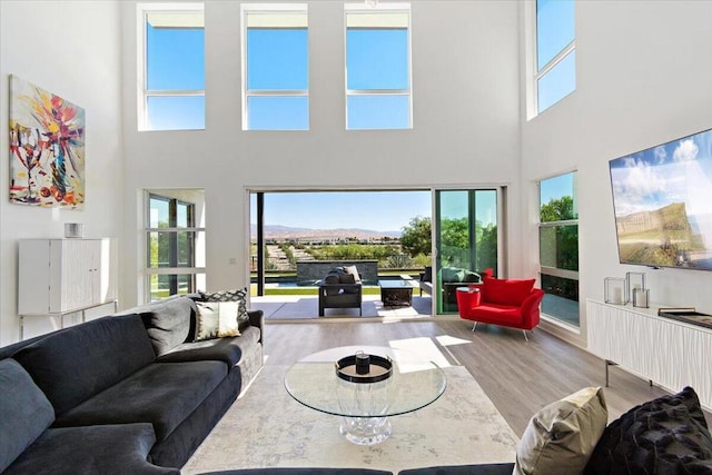 living room featuring light wood-type flooring, a towering ceiling, and plenty of natural light