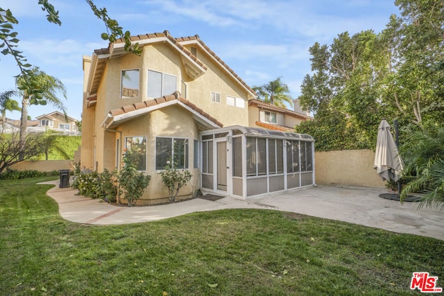 rear view of property featuring a sunroom, a patio area, and a lawn