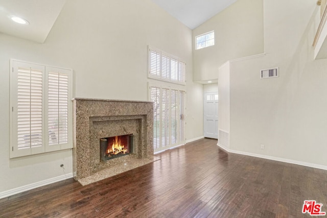 unfurnished living room featuring a wealth of natural light, a high end fireplace, dark wood-type flooring, and high vaulted ceiling