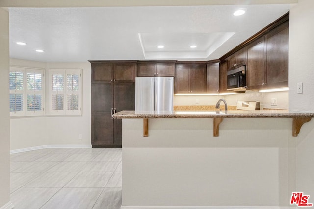 kitchen featuring light stone countertops, appliances with stainless steel finishes, dark brown cabinetry, and a breakfast bar area