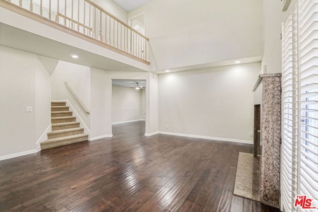 unfurnished living room featuring ceiling fan, dark hardwood / wood-style floors, and a high ceiling