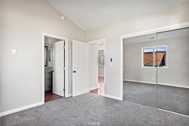 unfurnished bedroom with connected bathroom, vaulted ceiling, a closet, and dark colored carpet