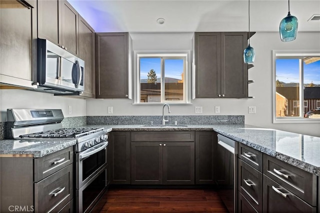 kitchen featuring sink, light stone counters, dark brown cabinets, appliances with stainless steel finishes, and pendant lighting