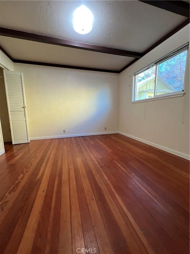 unfurnished room with wood-type flooring, a textured ceiling, and beam ceiling