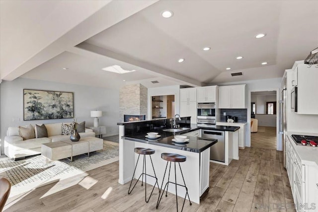 kitchen featuring light wood-type flooring, stainless steel appliances, sink, white cabinetry, and a breakfast bar area