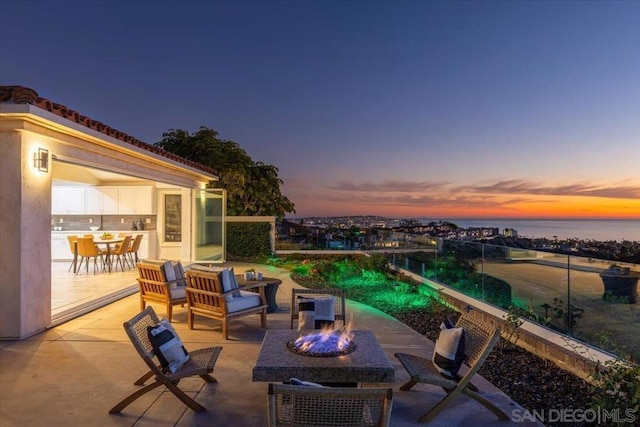 patio terrace at dusk with a water view and an outdoor living space with a fire pit