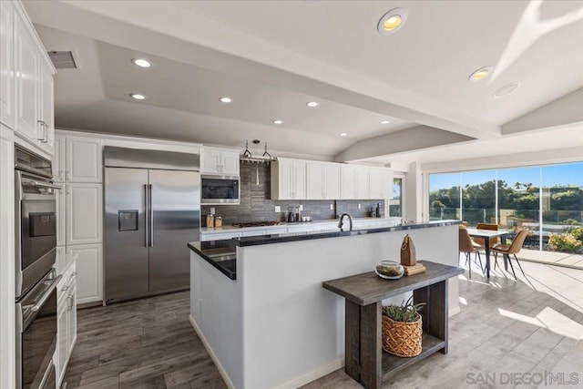 kitchen featuring white cabinets, vaulted ceiling, built in appliances, tasteful backsplash, and light hardwood / wood-style floors