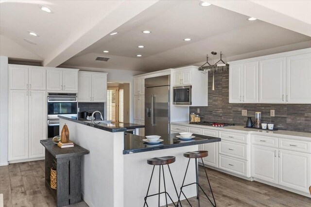 kitchen featuring a center island with sink, built in appliances, white cabinetry, and hardwood / wood-style flooring