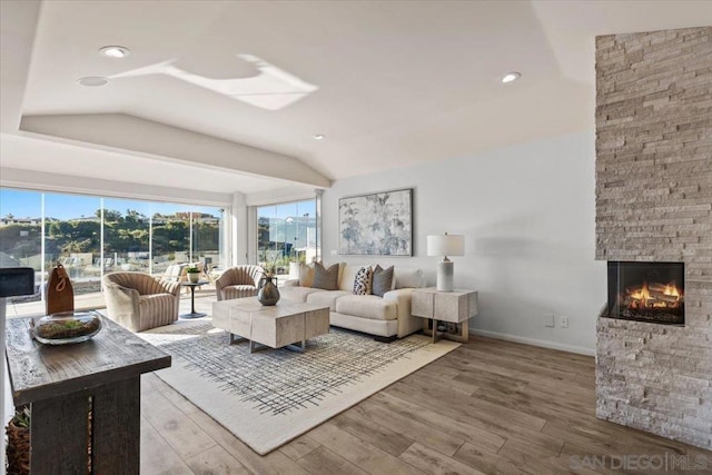 living room featuring a stone fireplace, lofted ceiling, and hardwood / wood-style flooring