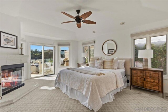 carpeted bedroom featuring access to exterior, ceiling fan, and a tiled fireplace