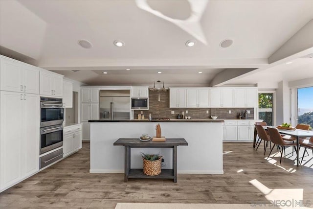 kitchen with built in appliances, a center island, white cabinets, and vaulted ceiling