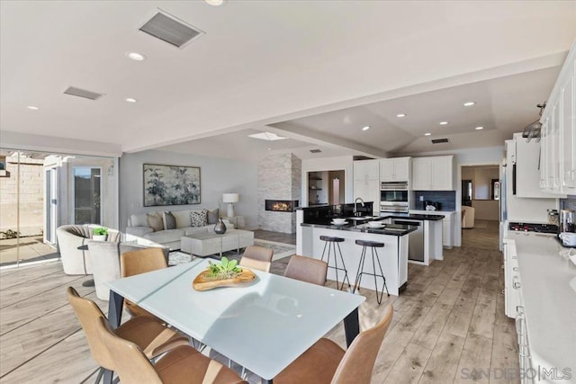 dining space with a fireplace, light wood-type flooring, lofted ceiling, and sink