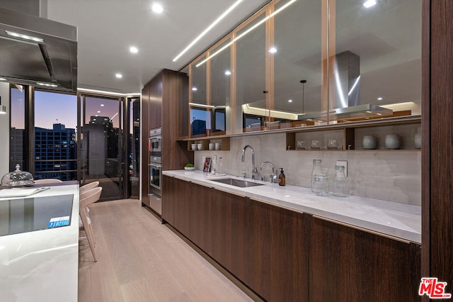 kitchen featuring oven, sink, light hardwood / wood-style flooring, tasteful backsplash, and dark brown cabinetry