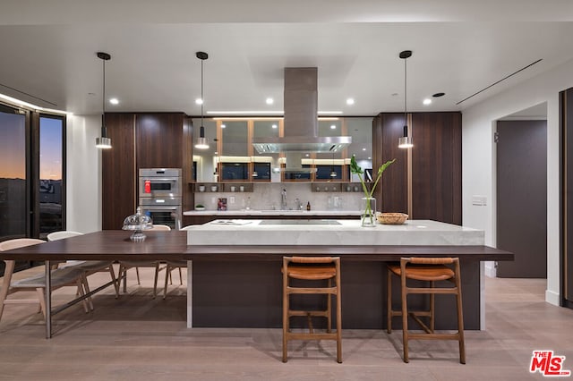 kitchen with dark brown cabinets, stainless steel double oven, island range hood, a spacious island, and hanging light fixtures