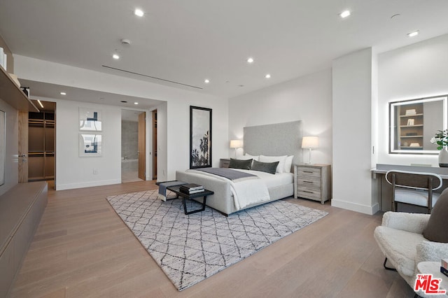 bedroom with ensuite bath, a spacious closet, and light hardwood / wood-style flooring