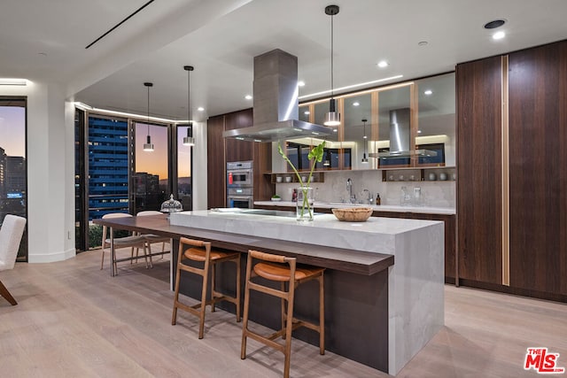 kitchen with backsplash, island range hood, light hardwood / wood-style flooring, and stainless steel appliances