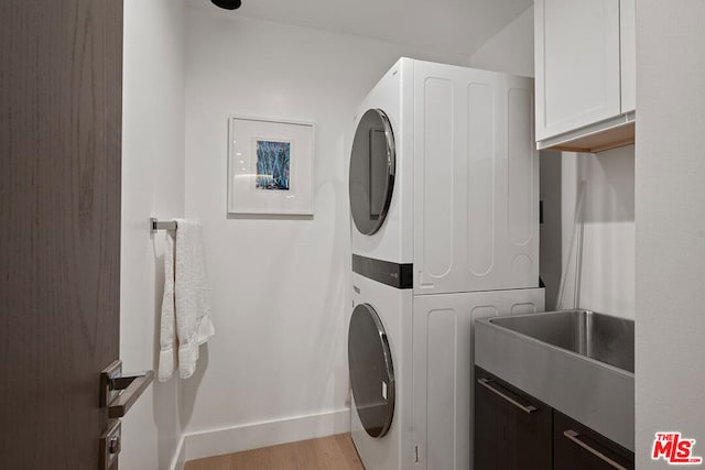 laundry room featuring cabinets, stacked washer and dryer, and light hardwood / wood-style flooring