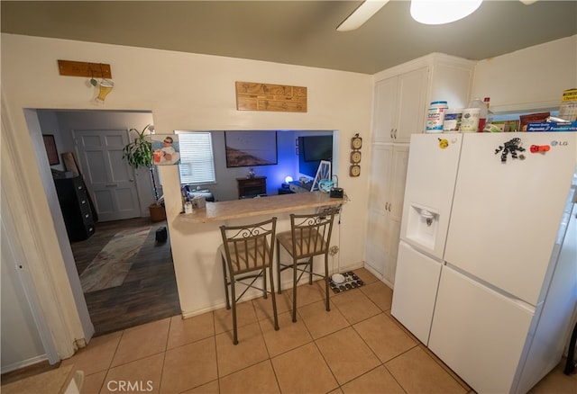 kitchen featuring a kitchen bar, ceiling fan, white refrigerator with ice dispenser, light hardwood / wood-style flooring, and white cabinets