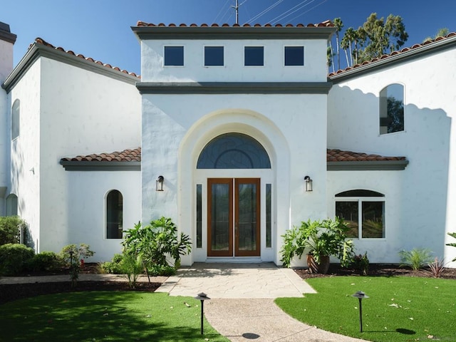 view of exterior entry featuring french doors and a lawn